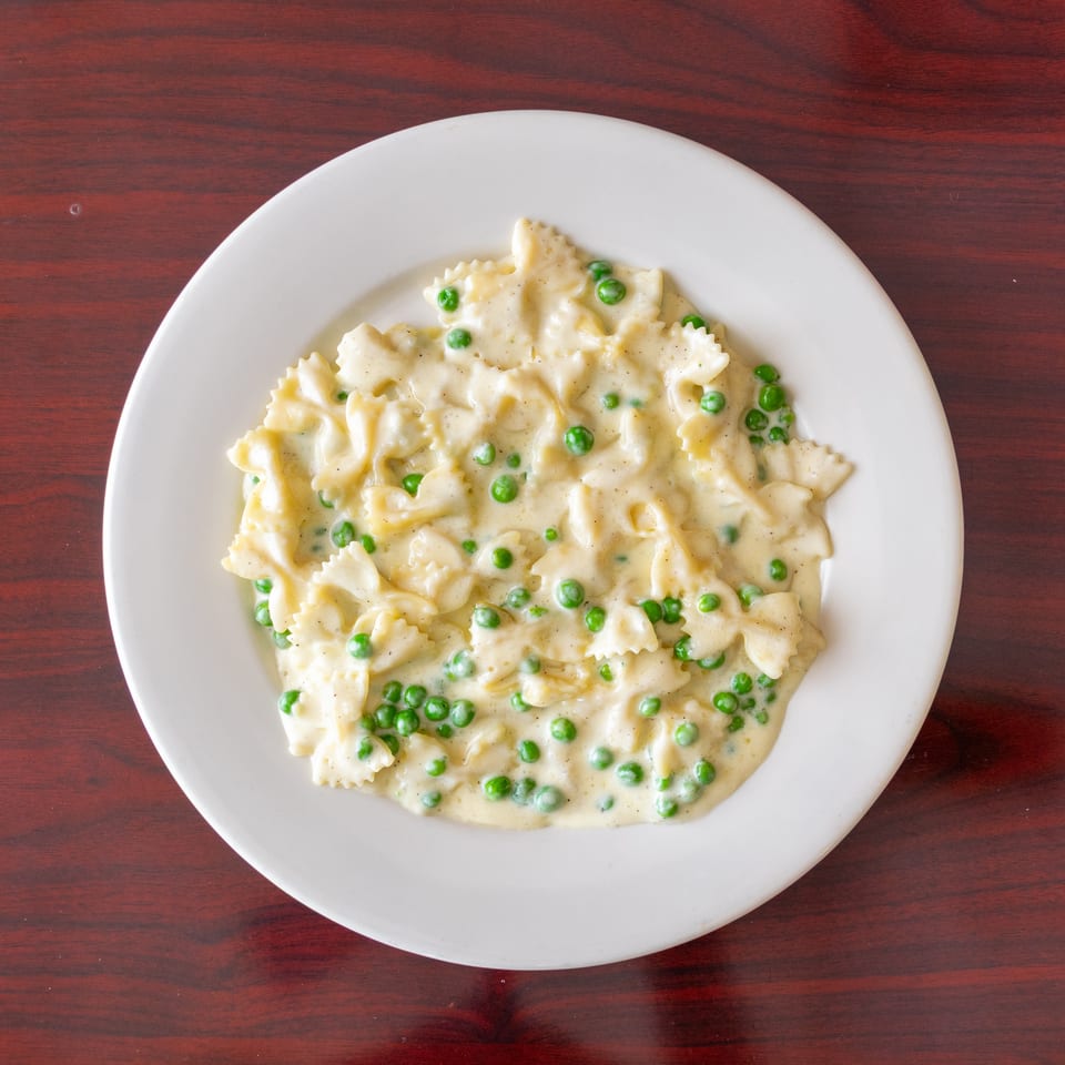 Creamy farfalle pasta with green peas served on a white plate atop a dark wooden table.