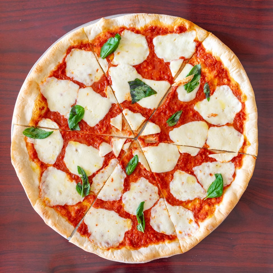Overhead view of a cheese pizza with tomato sauce and fresh basil on a dark wooden table.