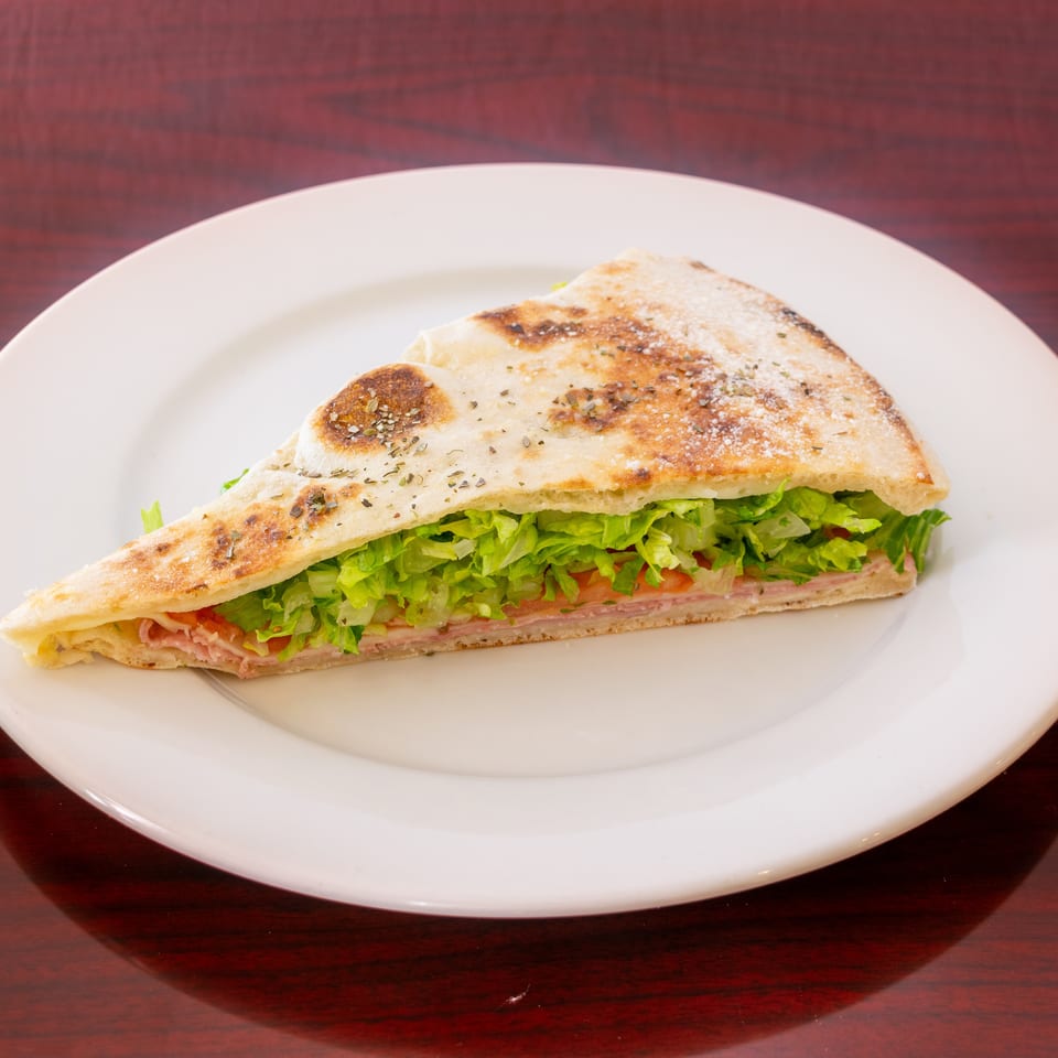 Grilled triangular sandwich filled with ham, lettuce, and tomato on a white plate.