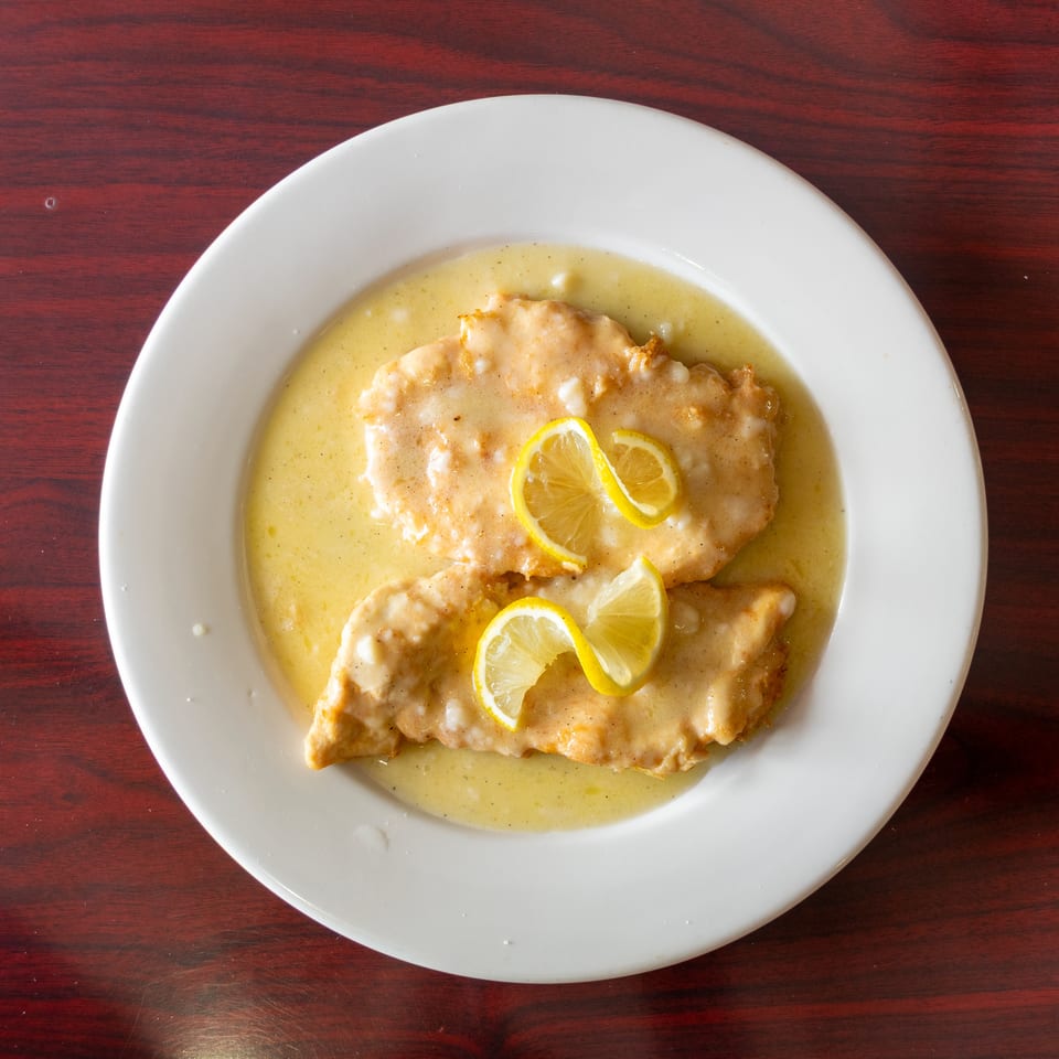Breaded chicken cutlets in lemon butter sauce, garnished with lemon slices on a white plate atop a wooden table.