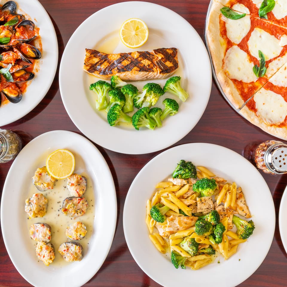Overhead view of Italian dishes including grilled salmon, mussels in tomato sauce, Margherita pizza, stuffed mushrooms, and chicken broccoli pasta.