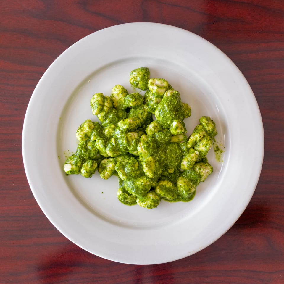 Gnocchi coated in vibrant green pesto sauce, served on a white plate atop a dark wooden table.