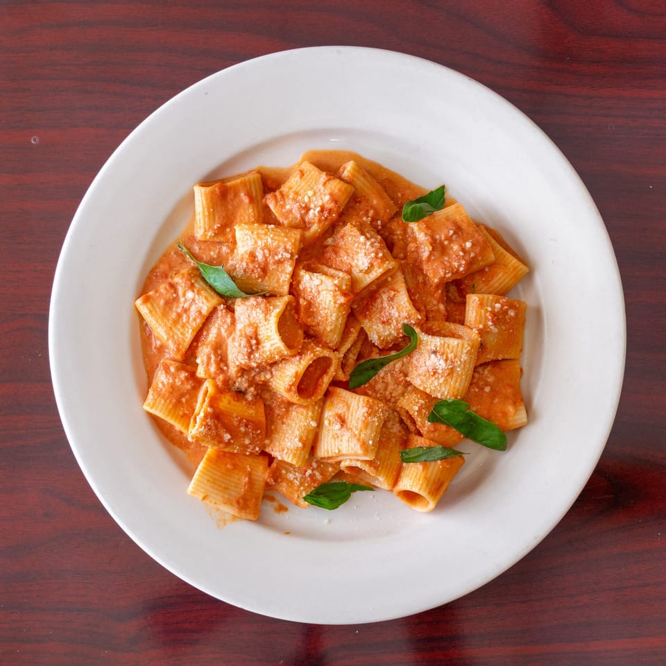Rigatoni pasta in creamy tomato sauce, topped with grated cheese and fresh basil on a white plate.