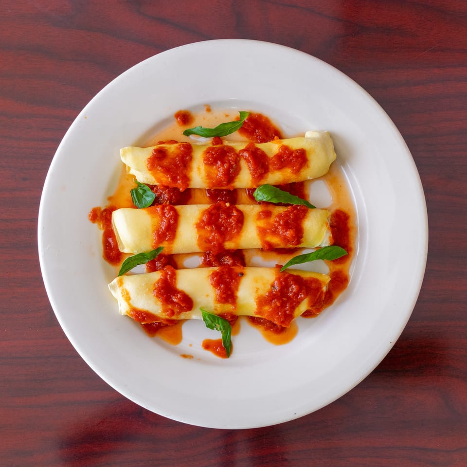 Three golden pasta rolls topped with tomato sauce and fresh basil leaves on a white plate.
