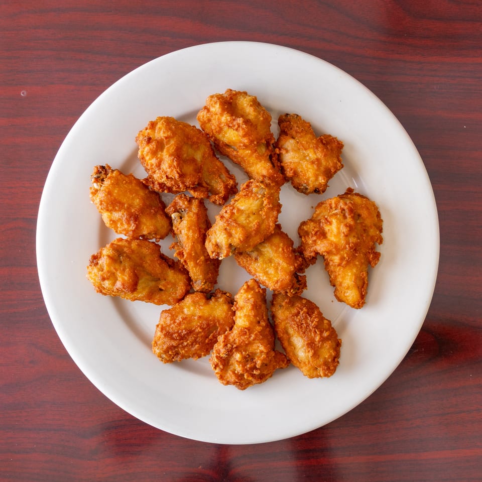 Golden-brown pieces of fried chicken arranged on a white plate over a reddish wooden table.
