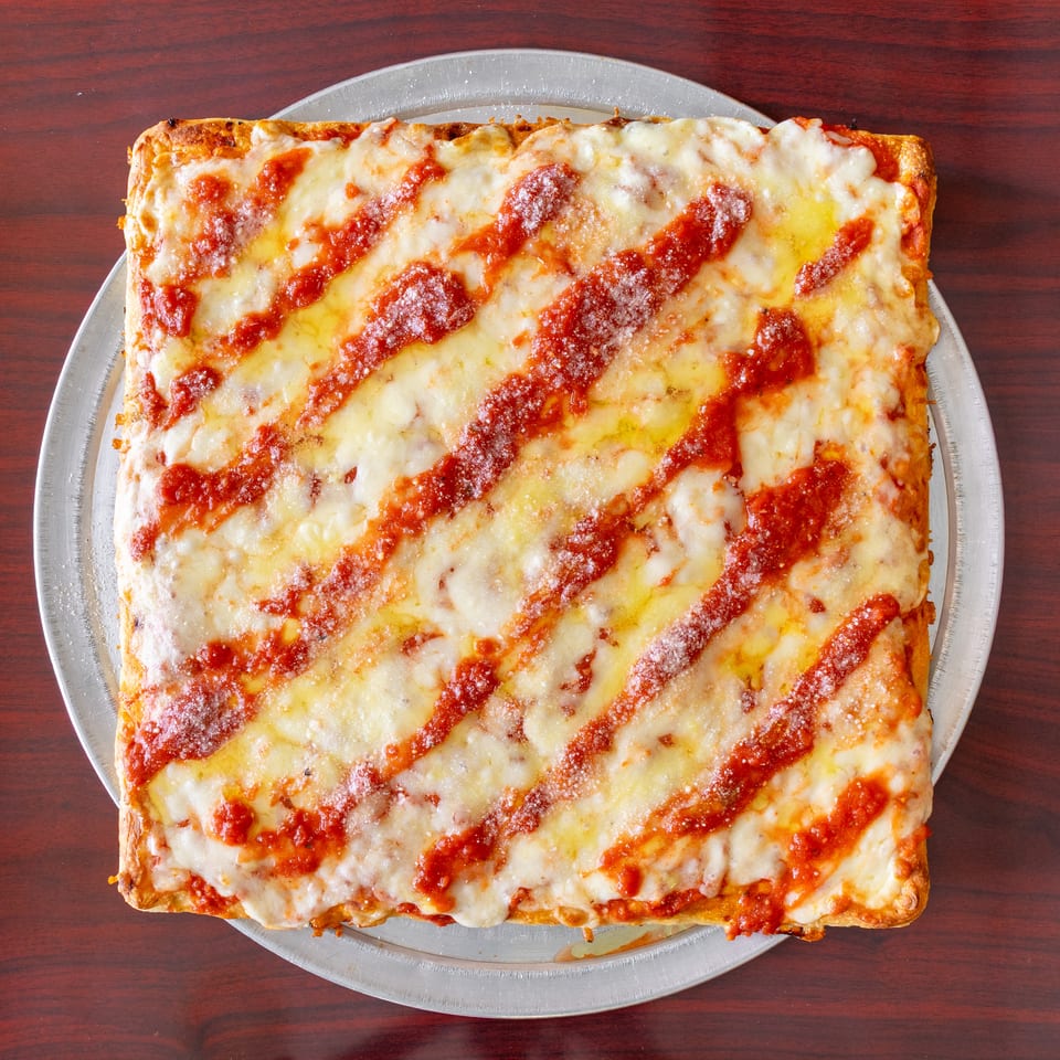 Rectangular cheese pizza with tomato sauce drizzled in diagonal stripes, served on a metal tray over a wooden table.